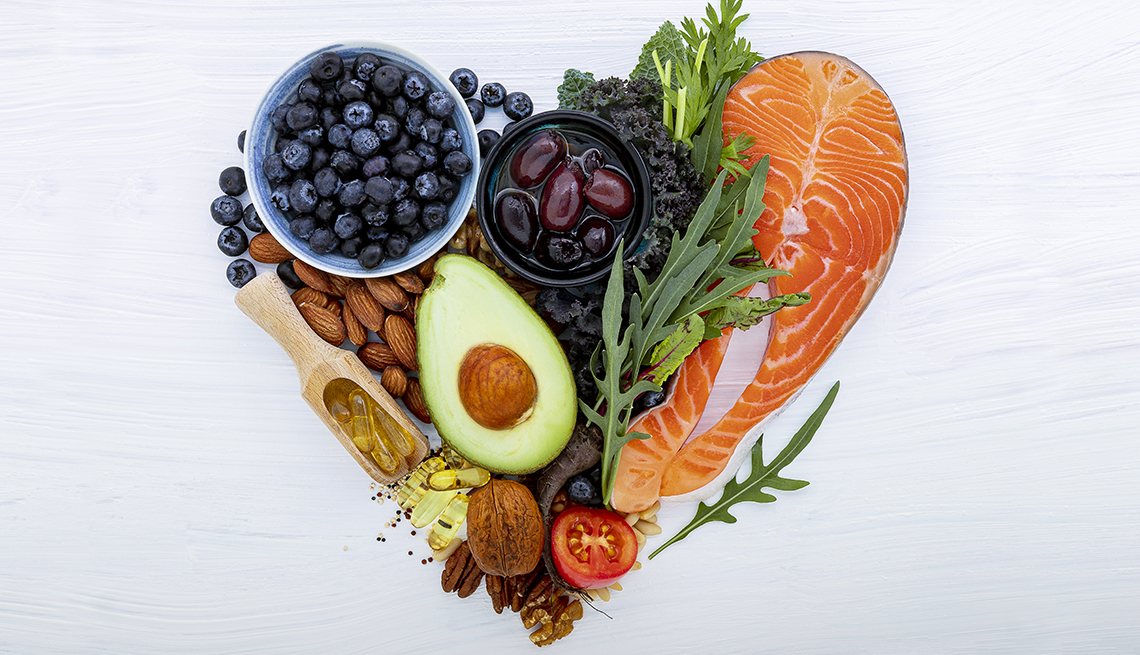 Alimentos saludables para el corazón que forman un corazón. Incluye arándanos, almendras, aguacate, aceitunas, frutos secos, salmón y vegetales