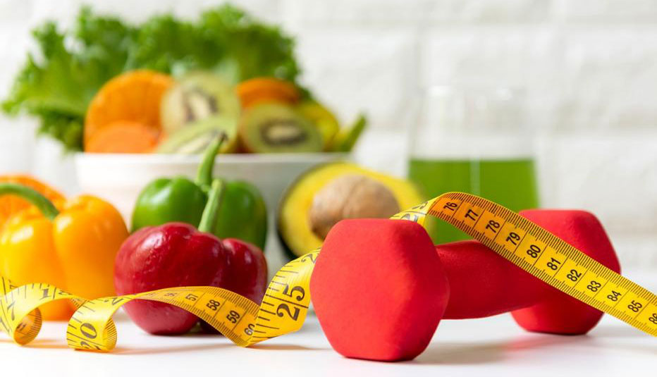 Vegetales, jugo verde, una pesa liviana y una cinta de medir sobre una mesa